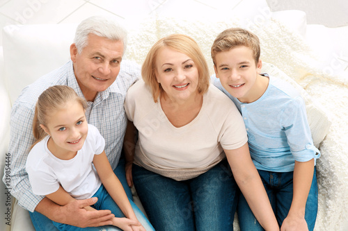 Cute children with grandparents sitting on sofa in living room