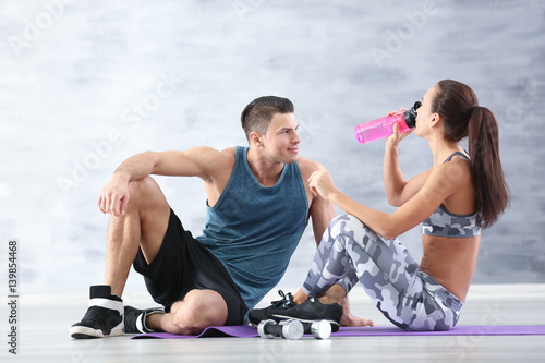 Young sporty couple drinking water after training in gym
