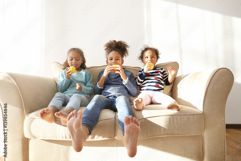 Three cute African girls sitting on sofa and eating lemons Three cute African girls sitting on sofa and eating lemons