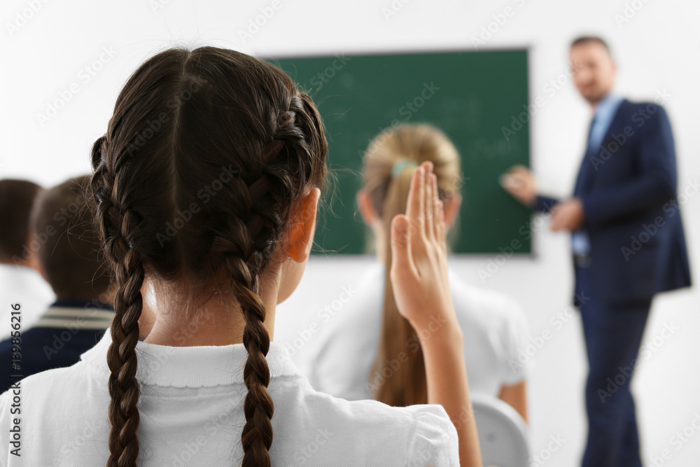 Fototapeta premium Schoolgirl raising hand for answer during lesson
