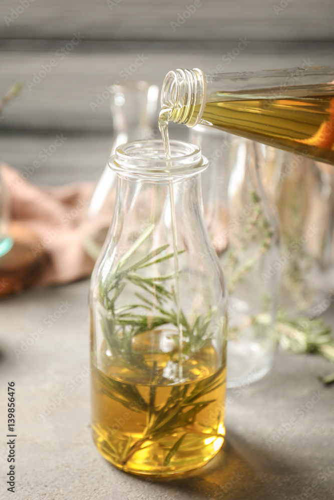 Pouring oil into bottle with rosemary on table Pouring oil into bottle with rosemary on table