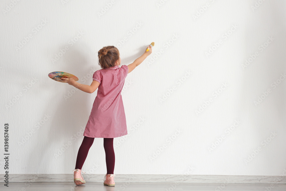 Fototapeta premium Cute little girl painting on wall in empty room