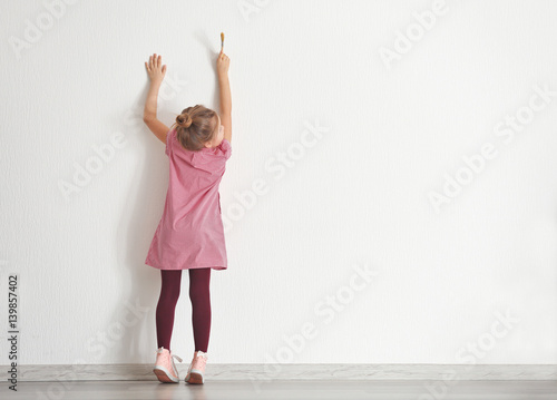 Fototapeta Naklejka Na Ścianę i Meble -  Cute little girl painting on wall in empty room
