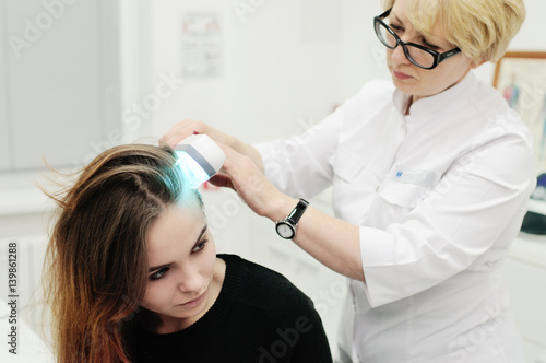 Doctor examines scalp a pretty young girl with special instrument UV lamp. Skin problems, dermatology, shingles, psoriasis, redness, prevention