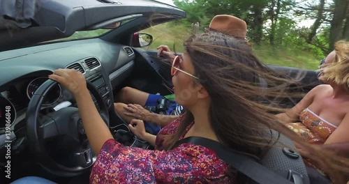 Beautiful young woman dressed in boho style driving her friends in convertible