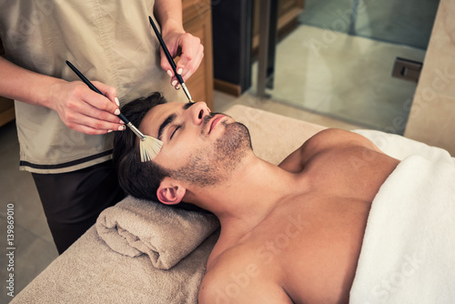 Man lying down during traditional facial treatment at beauty center photo