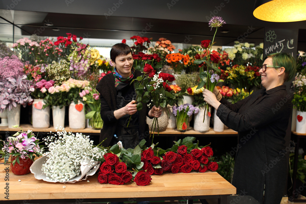 Dwie uśmiechnięte kobiety w kwiaciarni robią bukiety z kwiatów ciętych. - obrazy, fototapety, plakaty 