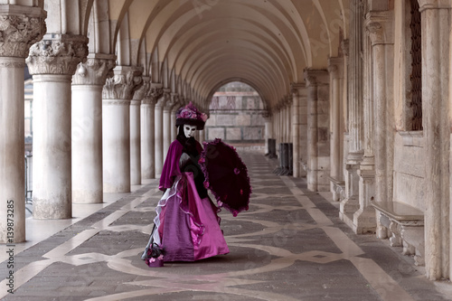 Lonely lady in violet costume in the colonnade of Doge's Palace at Carnival in Venice