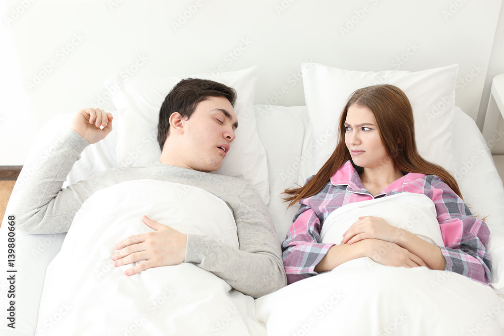 Fototapeta premium Young irritated woman lying in bed with snoring husband at home