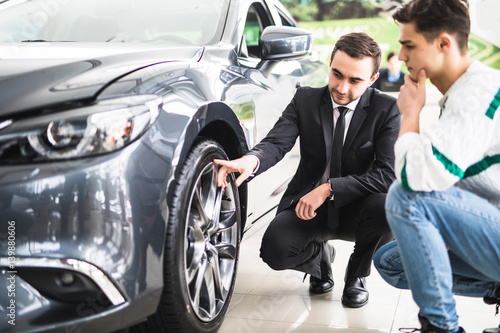 Young car salesman showing the advantages of the car to the customer and tires.