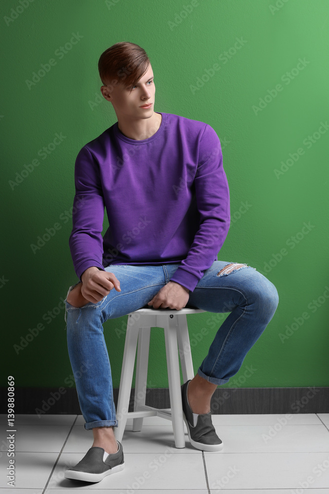 Handsome young man sitting on stool near color wall Handsome young man sitting on stool near color wall