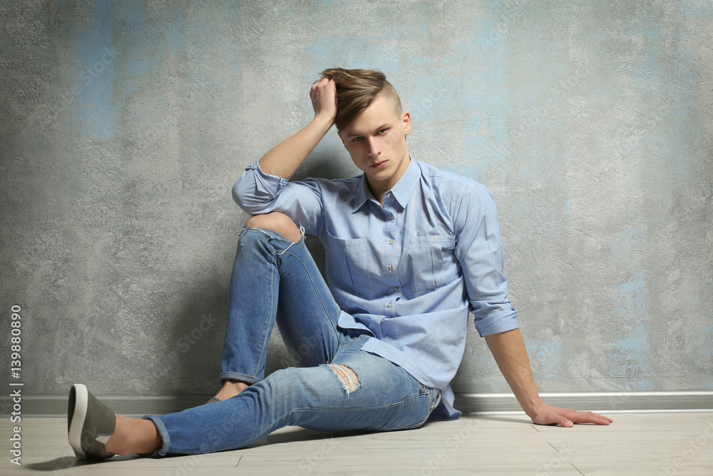 Handsome young man sitting on floor near textured wall Handsome young man sitting on floor near textured wall