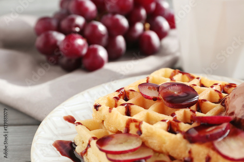 Tasty waffles with delicious grape, ice-cream and syrup on white plate, close up
