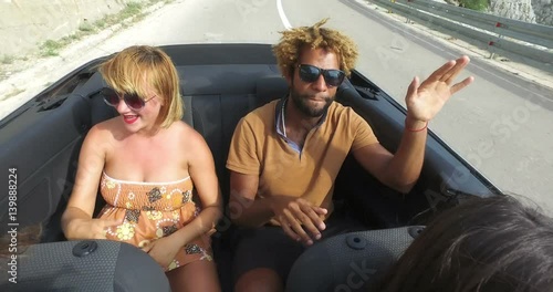 Four young hipster friends having fun riding in convertible
