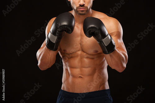 Muscular young man with perfect Torso with six pack abs, in boxing gloves is showing the different movements and strikes isolated on black background with copyspace © satyrenko