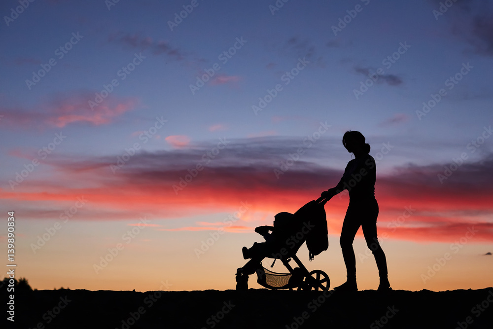 Silhouette mother pulling baby stroller against beach sunset. Silhouette mother pulling baby stroller against beach sunset.