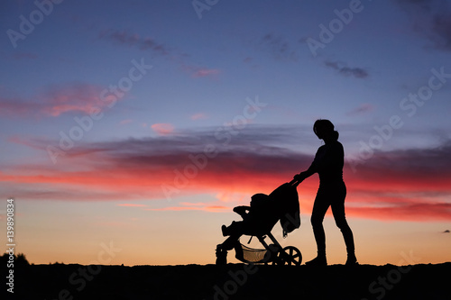 Silhouette mother pulling baby stroller against beach sunset.