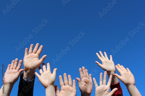 Row of hands with open palms on blue sky background