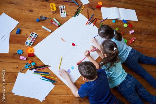 children lying on the floor and drawing. Children draw on a large sheet of paper