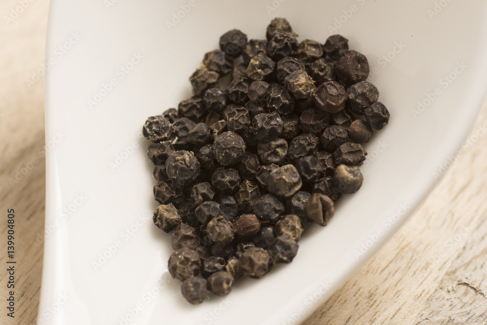 black pepper in white spoon on wooden background black pepper in white spoon on wooden background