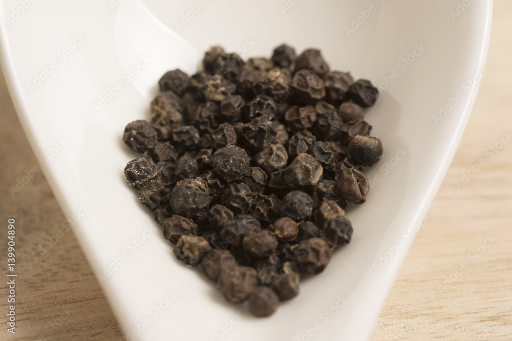 black pepper in white spoon on wooden background black pepper in white spoon on wooden background