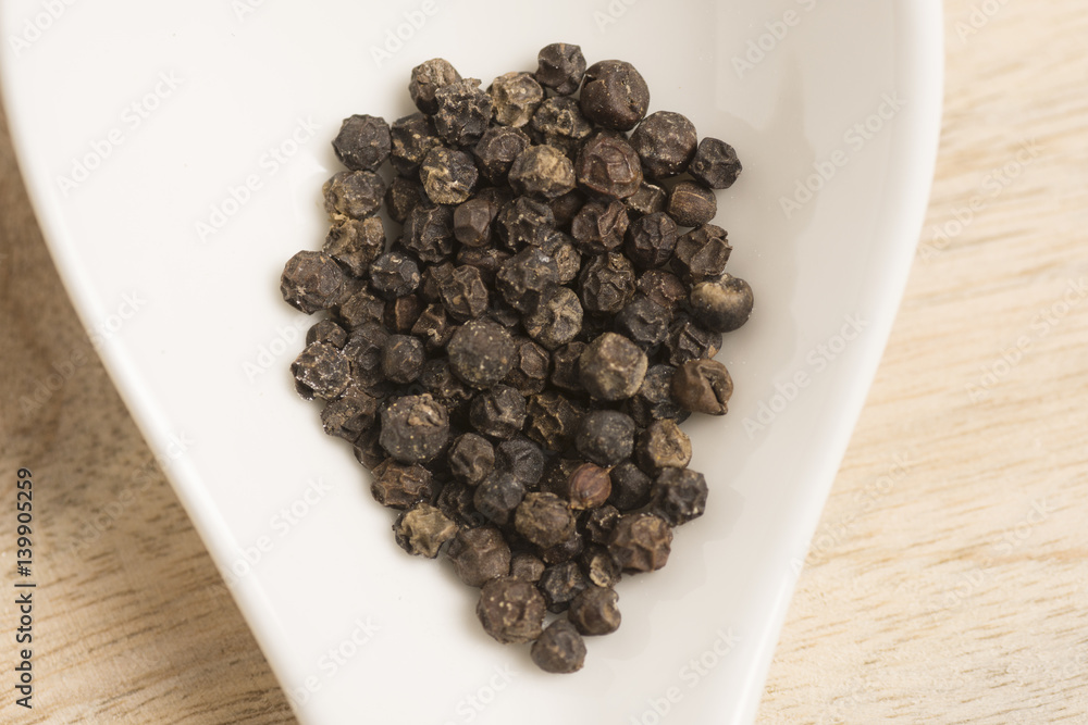 black pepper in white spoon on wooden background black pepper in white spoon on wooden background
