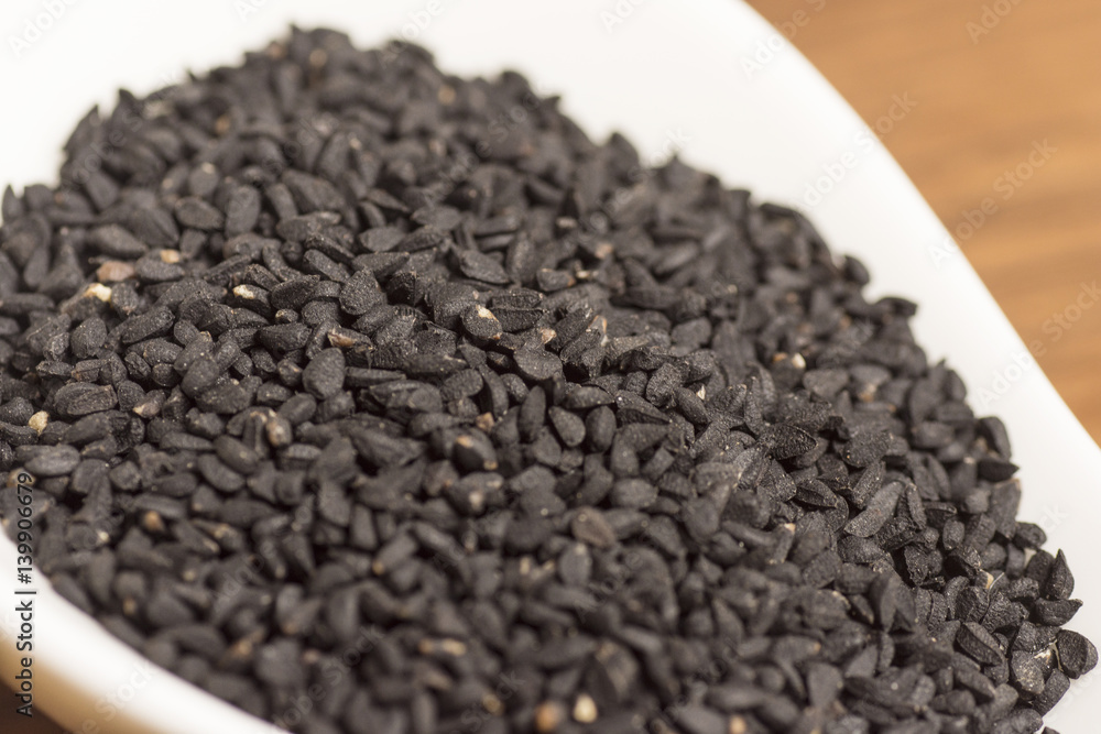black seeds in white spoon on wooden background black seeds in white spoon on wooden background