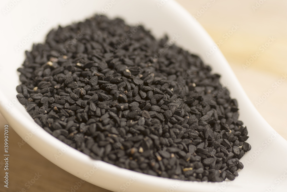 black seeds in white spoon on wooden background black seeds in white spoon on wooden background