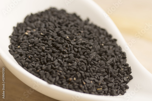 black seeds in white spoon on wooden background
