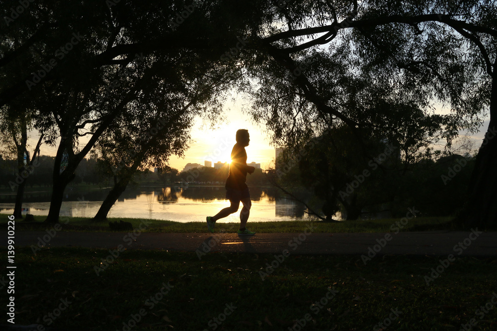 Silhouette of person jogging in park during morning sunrise