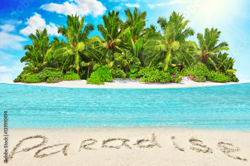 Whole tropical island within atoll in tropical Ocean and inscription "Paradise" in the sand on a tropical island.