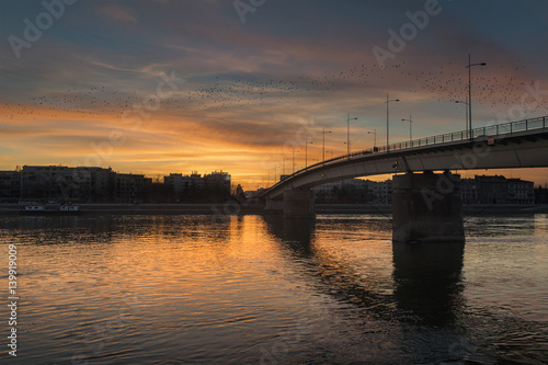 Beautiful warm sunset on the city panorama with buildings and colorful sky over the bridge and river