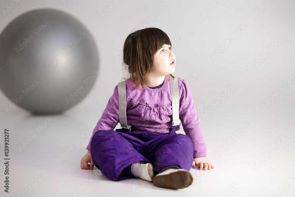 little girl in purple clothes with big ball for fitness on gray 