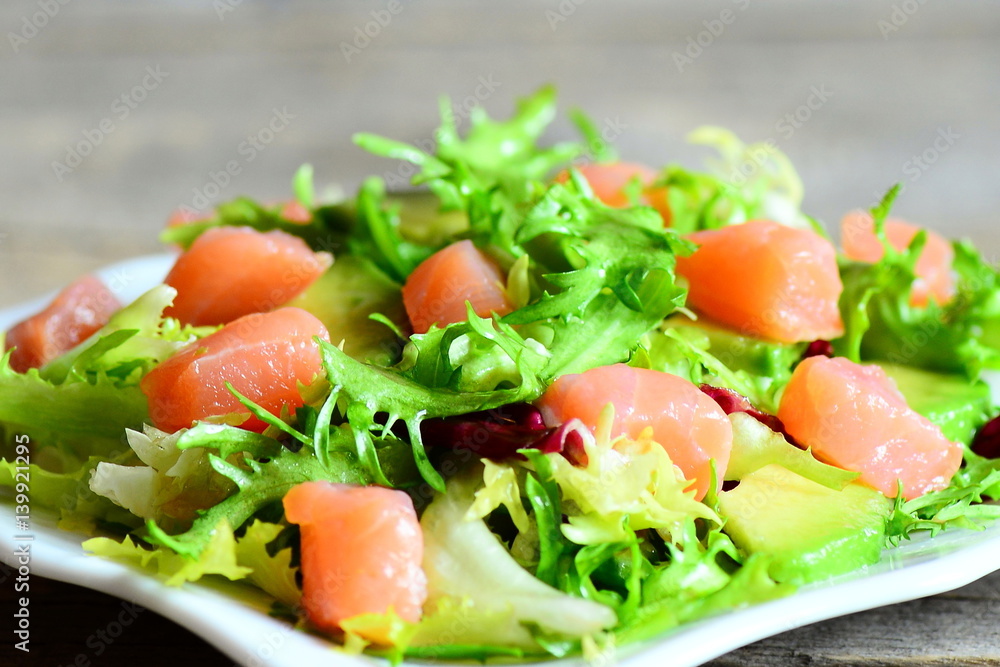 Salmon, avocado and lettuce salad. Healthy salad with slices of salmon, fresh avocado and lettuce leaves mix on a plate. Closeup