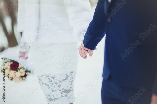 The bride and groom are gently holding hands at the wedding, close-up in the winter