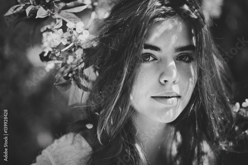 Beautiful young brunette girl in a blooming cherry orchard. Black-and-white picture. Close-up.