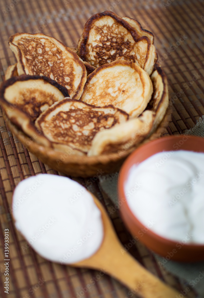 Cooked homemade pancakes on a dining table in a wicker plate next to sour cream for breakfast. Sweet dessert. Homemade cooking. With your own hands. Homemade Cooked homemade pancakes on a dining table in a wicker plate next to sour cream for breakfast. Sweet dessert. Homemade cooking. With your own hands. Homemade