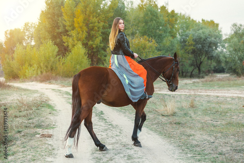 A beautiful girl is walking her horse. Focus on the girl. The warm tone of the image. Soft focus.