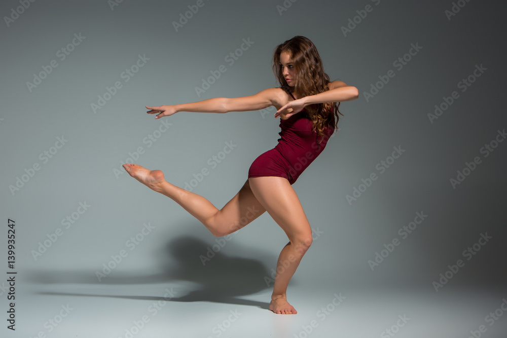 Young beautiful woman in red T-shirt and shorts dancing on a dark gray studio background