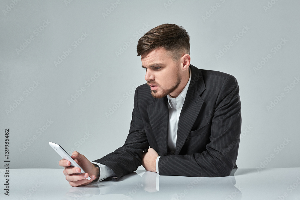 Handsome young man talking on the mobile phone while sitting at his working place in office Handsome young man talking on the mobile phone while sitting at his working place in office