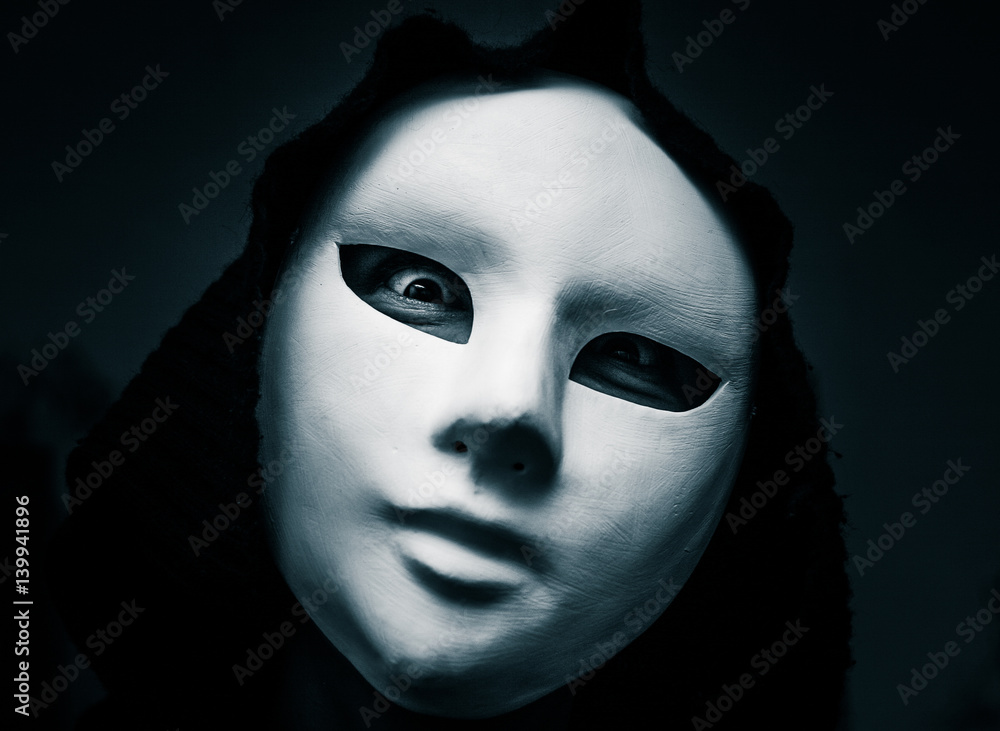 Artistic, monochrome picture of a white carnival mask weared by a woman in darc clothes