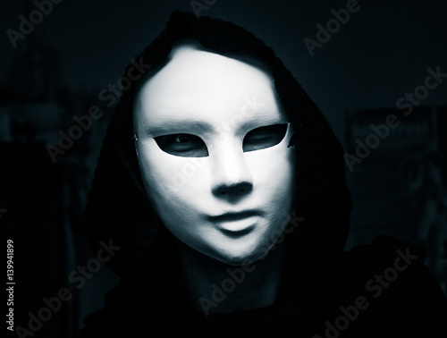 Artistic, monochrome picture of a white carnival mask weared by a woman in darc clothes photo
