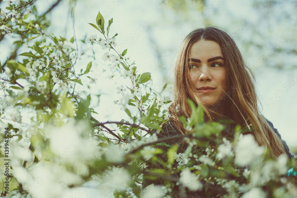 Happy smiling young woman in a knitted jacket enjoying spring flowers in the garden Happy smiling young woman in a knitted jacket enjoying spring flowers in the garden