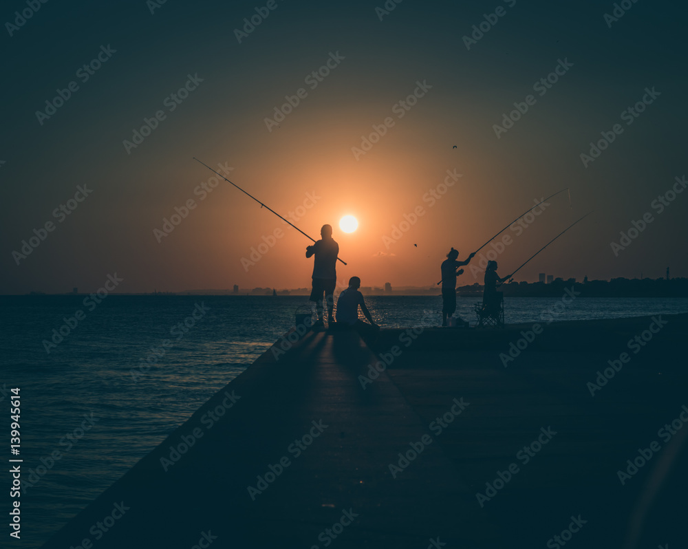 Silhouettes of fishermen by the sea at sunset