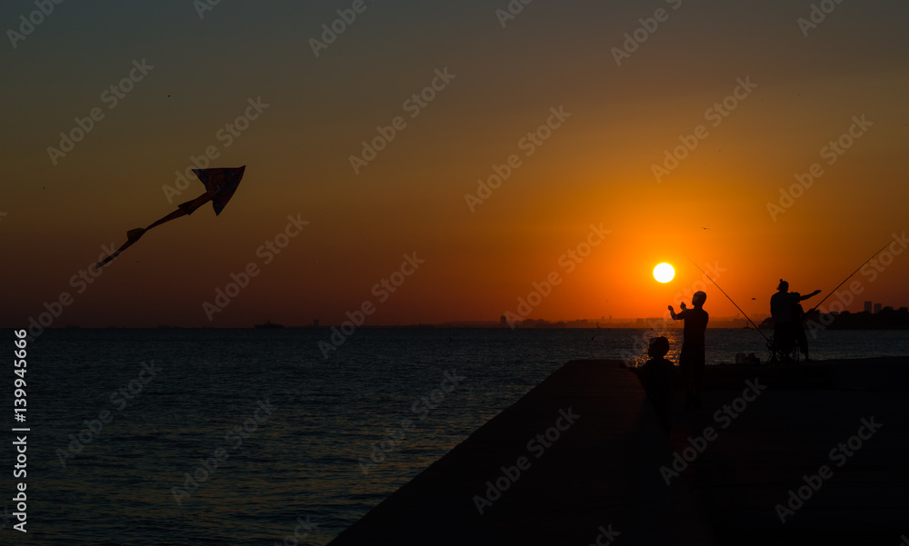 Obraz premium Silhouettes of father and son flying a kite in sunset