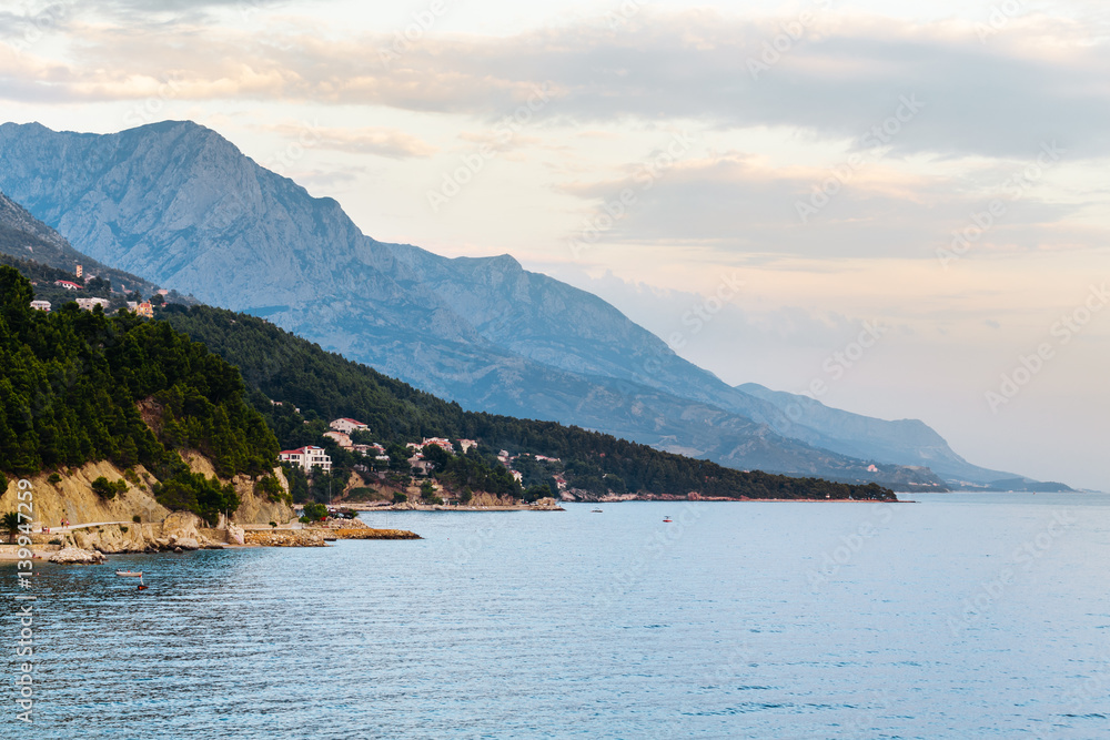 Evening coastline with rocks, trees and mountains in Brela, Croatia at the Adriatic Sea.