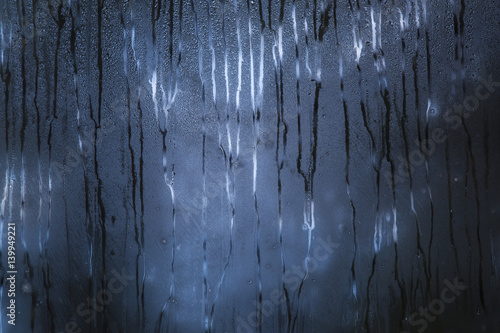 Dark blue rainy window with scary pattern of the raindrops paths