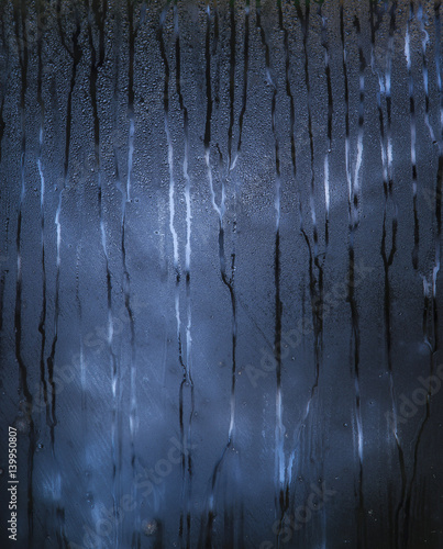 Dark blue rainy window with scary pattern of the raindrops paths