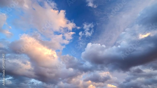 Time-lapse footage of blue sky full of golden clouds during colorful sunset.