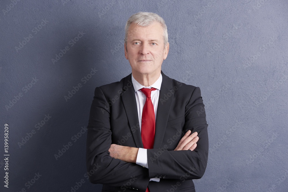 Confident senior businessman standing against grey wall Confident senior businessman standing against grey wall
